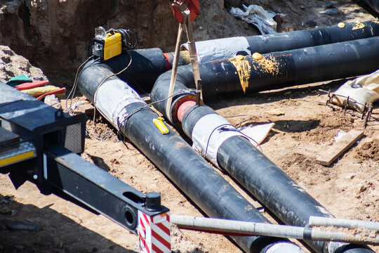 Heating mains pipes installation work in open trench on construction site, featuring equipment and machinery element for utility infrastructure repair and relocation