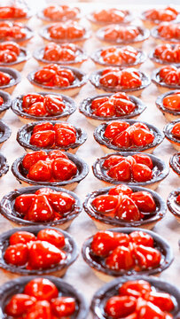 Neatly arranged rows of freshly baked mini strawberry tarts displaying vibrant red fruit topping, dark chocolate crusts, and glistening fruit glaze, perfect for dessert display, vertical photo