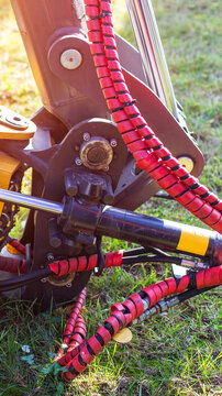 Close-up of hydraulic system of heavy construction machinery featuring strong metal components and protective red coiled hoses on green grass, sunlight effect, vertical photo