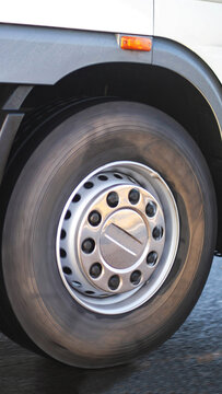 Close up view of moving truck wheel on road, showing tire, rim, and lug nuts with motion blur effect, transportation industry concept, vertical photo