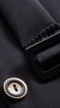Close-up detail of black fabric garment featuring decorative gold and black button with textured surface and sleek black plastic buckle element vertical photo