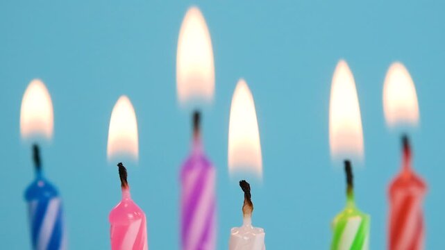 Colorful birthday candles burning and blowing out with flickering flames and smoke against a bright blue background, slow motion video.