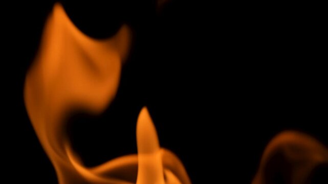 Close-up of orange fire flames moving and flickering in darkness on a black background. Glowing heat and burning flame texture. Slow motion video.
