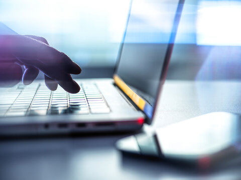 Male hand types data on a laptop keyboard indoors