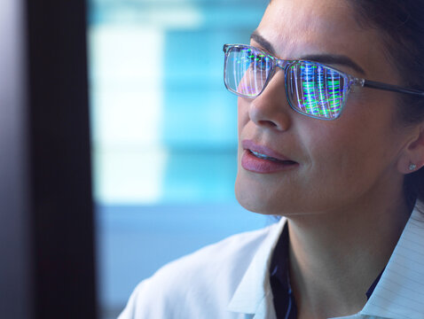 A female scientist analyzes DNA data reflecting in her glasses