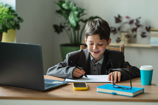 Smiling boy in a suit playing businessman writing at an office desk