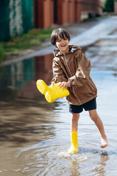 A smiling boy empties water from his yellow boot into a street puddle