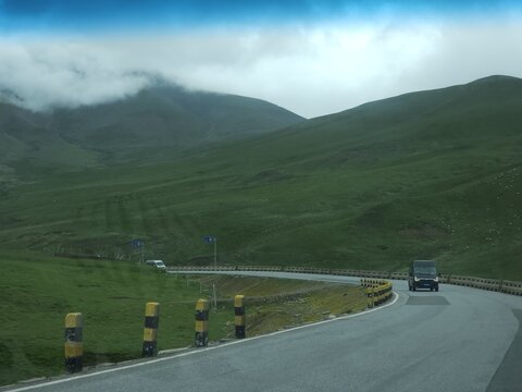 Hainan Tibetan Autonomous Prefecture, Qinghai, China - 04 August 2026: View of Laji Mountain with a winding road cutting through lush green hills under a cloudy sky.