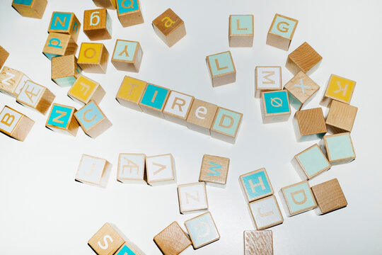 Wooden building blocks spell the word tired on a white background