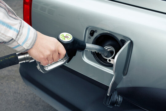 Hand holding fuel nozzle to refuel car with green energy