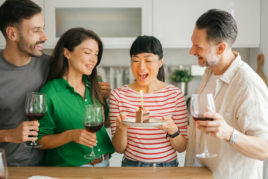 Friends celebrating birthday with cake and wine in kitchen