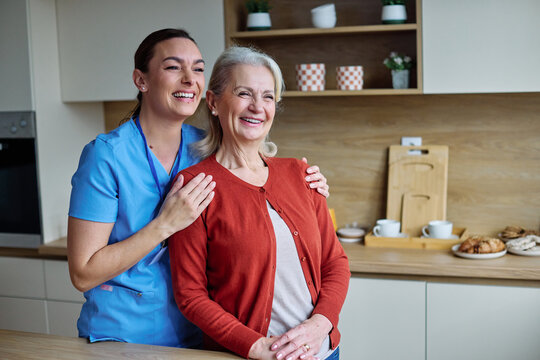 Portrait of a doctor or nurse caregiver supporting senior woman, hugging and bonding in kitchen at home or nursing home