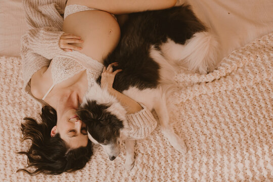 Pregnant woman hugging her border collie dog on a cozy bed indoors