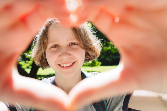 Smiling girl frames her face with a heart gesture outdoors