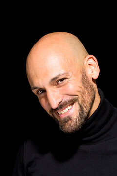 Portrait of smiling bald man with wearing black turtleneck in front of black background