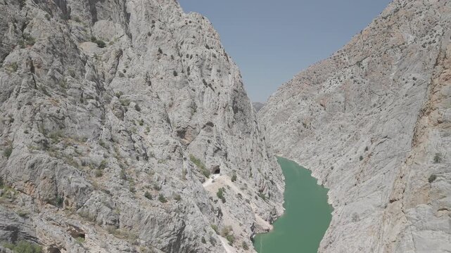 4K 10-bit drone pull-back shot flying backward inside the narrow Dark Canyon revealing hand-carved stone tunnels and window openings in Turkey