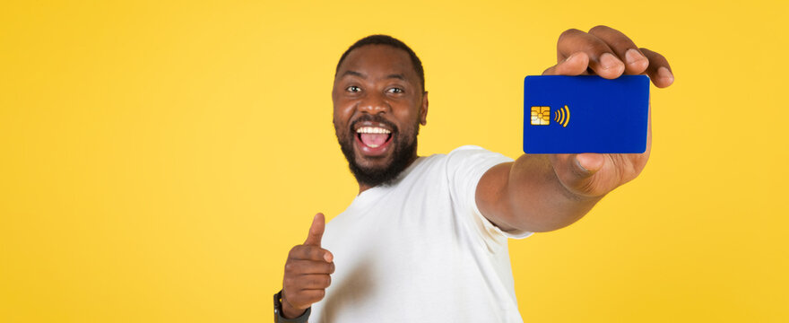 Cheerful Black Man Smiling While Holding Contactless Payment Card Against Bright Yellow Background, Promoting Modern Payment Solutions And Technology At Home.