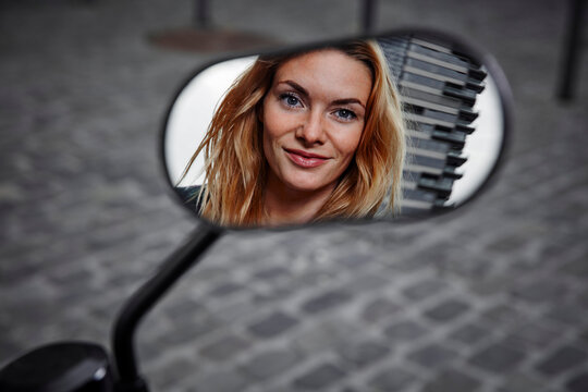 Portrait of smiling young woman reflected in wing mirror of a motorcycle