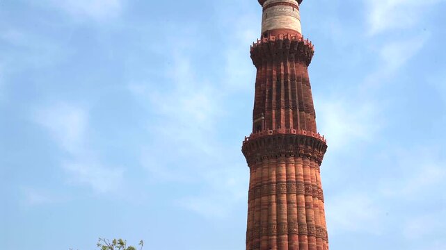 Static low angle close up shot of the upper balconies and detailed carvings of Qutub Minar minaret against a blue sky in New Delhi, India.