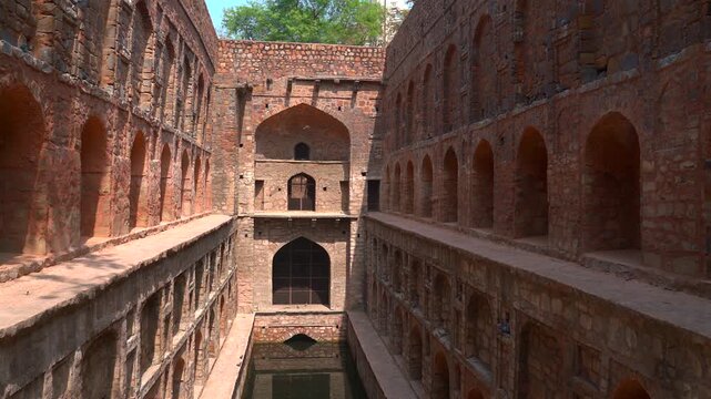 Pan wide shot of the historic red sandstone arches and water reservoir at Agrasen Ki Baoli stepwell in New Delhi, India.