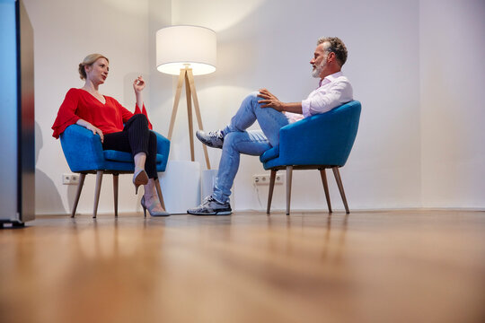 Mature man and young woman sitting in armchairs talking