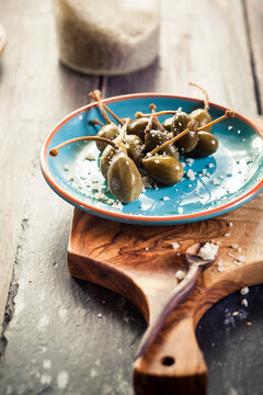Pickled caperberries, Capparis spinosa, with sea salt on plate, studio