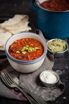 Tortillas and bowls of guacamole, sour cream, Chili con carne on wooden table
