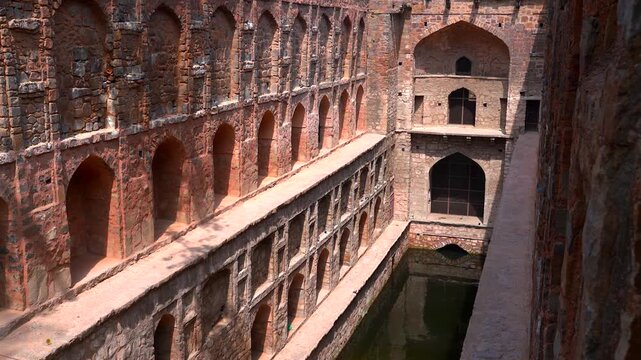 Static wide shot of the historic stone arch corridors and deep water reservoir at Agrasen Ki Baoli stepwell in New Delhi, India.
