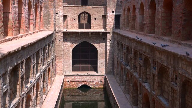 Camera tilting up from the water reservoir to reveal ancient red sandstone arches at Agrasen Ki Baoli stepwell in New Delhi, India.