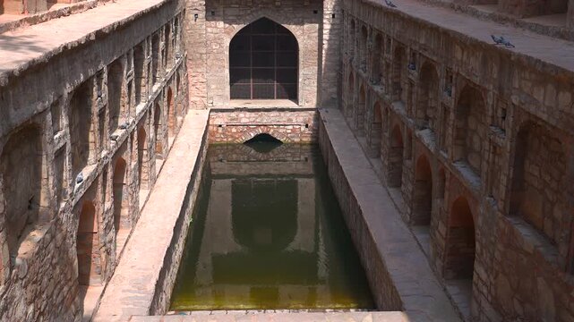 Static high angle wide shot of the ancient red sandstone arches and water pool at Agrasen Ki Baoli stepwell in New Delhi, India.