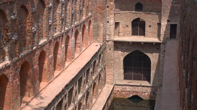 Tilting down shot along ancient red sandstone arches to reveal the water pool at Agrasen Ki Baoli stepwell in New Delhi, India.