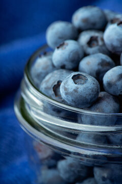 Glass jar with blueberries on blue textured fabric. Dark background.