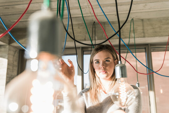 Young businesswoman in office examining cables at light bulbs