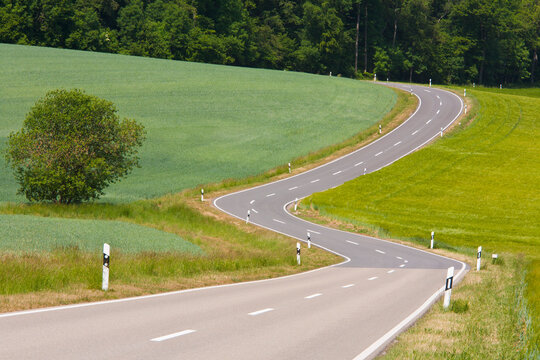 A twisting country road winds through green fields in Germany