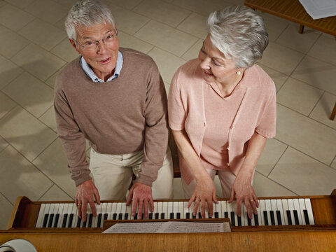 Senior man and woman play the piano together in a retirement home