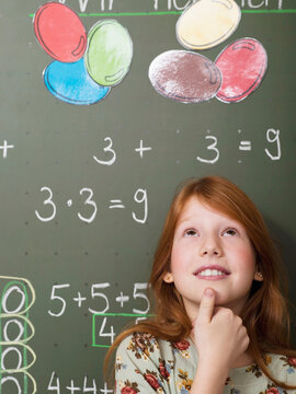 Girl (6-7) standing in front of blackboard, looking upward