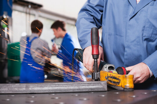 Germany, Neukirch, Person using grinder, Apprentice and foreman in background