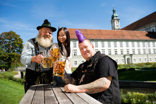 Germany, Bavaria, Upper Bavaria, Three people in beer garden holding beer stein glasses, smiling