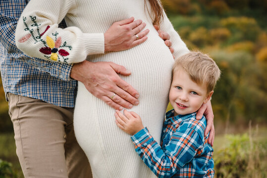 Photo family closeup in autumn. Family portrait outdoors in autumn. A pregnant woman, man, and their little son standing together on a scenic hill with a forest background, embracing.