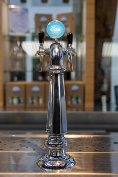 Enkhuizen, Netherlands - July 13, 2026: Chrome water tap labeled &ldquo;Eau&rdquo; at a bar counter, with restaurant interior and packaged products softly blurred in the background.