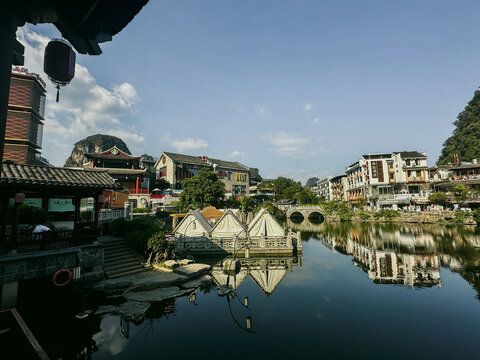 Guilin, Guangxi, China - 10 October 2024: View of Yangshuo County waterfront with traditional architecture, calm river reflections, and karst mountains under a clear blue sky.
