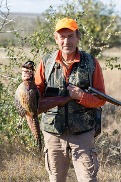 A hunter holds a pheasant in his hands. A successful hunt, a trophy game.