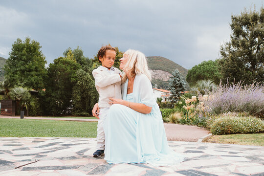 Grandmother gently interacts with her young grandchild outdoors. Both display happy expressions, with lush greenery and garden elements in the background, highlighting their special bond.
