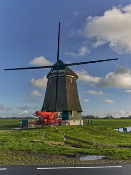 Obdam, North Holland, Netherlands - 25 November 2022: View of the historic drainage mill of the Berkmeer polder with its renovated iron stocks and sails in a green field.