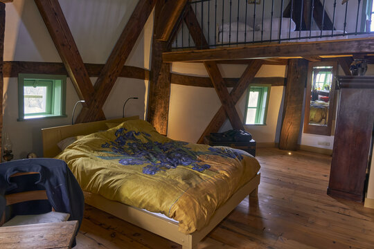 Waarland, Netherlands - 25 November 2022: View of the interior of the Slootgaarpolder mill, featuring a cozy bedroom with exposed wooden beams, a bed with a floral duvet, and a loft area.