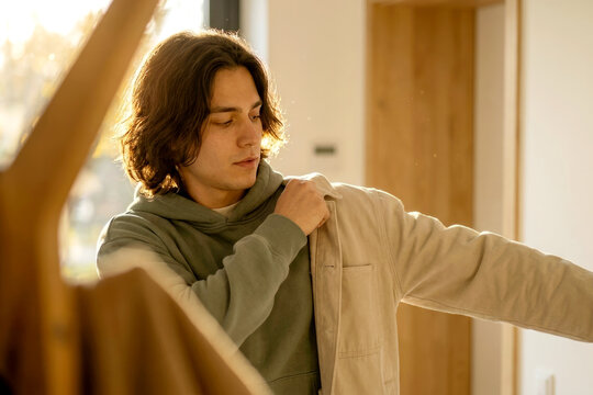 Young man putting on jacket at home in golden morning light
