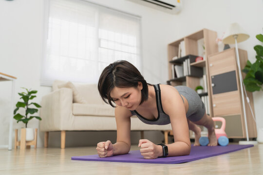 Woman Performing Core Strengthening Exercise on Yoga Mat in Living Room with Bookcase and Potted Plant