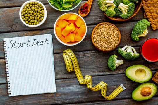 Diet program mockup. Start diet text in notebook near vegetables on dark wooden background top view