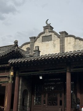 Xi An Shi, Shan Xi Sheng, China - 02 August 2026: View of the Great Mosque of Xi'an featuring traditional wooden architecture, roof tiles, and a crescent moon symbol under a cloudy sky.