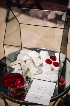 Elegant glass box for wedding wishes or cards, featuring white decorative stones, red wax seals, and romantic "I am yours, you're mine" cards. A sophisticated detail for a luxury event setup.